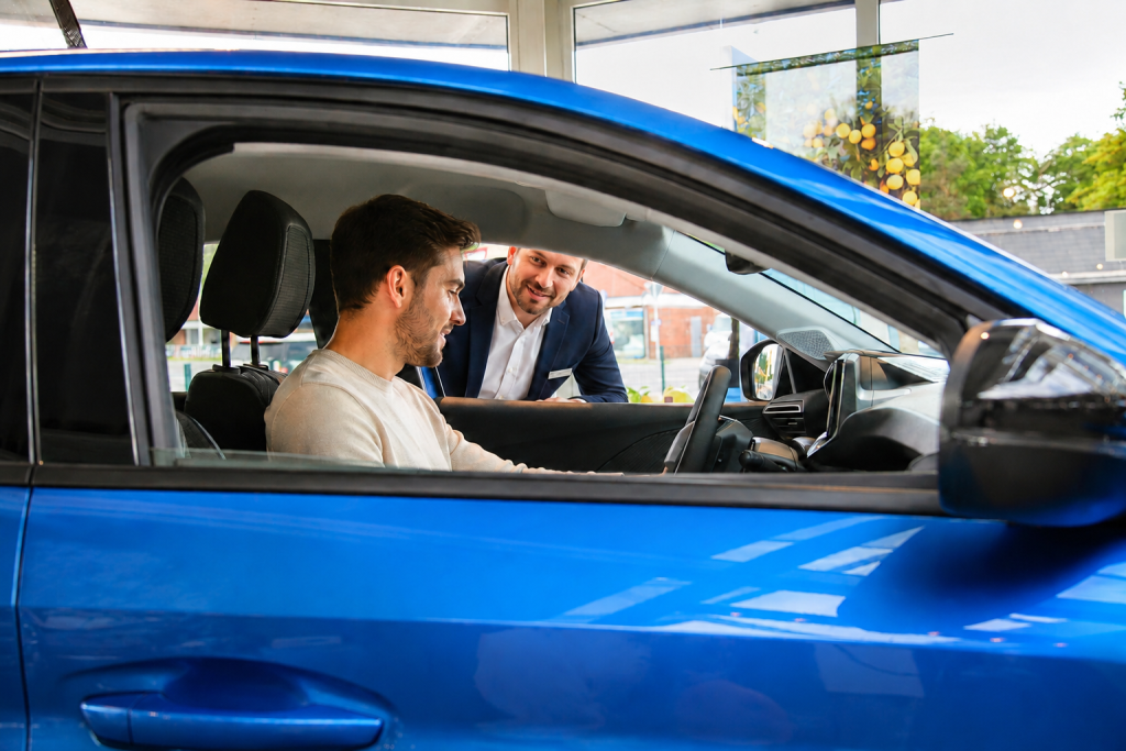 Ein Verkäufer berät einen Kunden im Inneren eines blauen Peugeot-Fahrzeugs.
