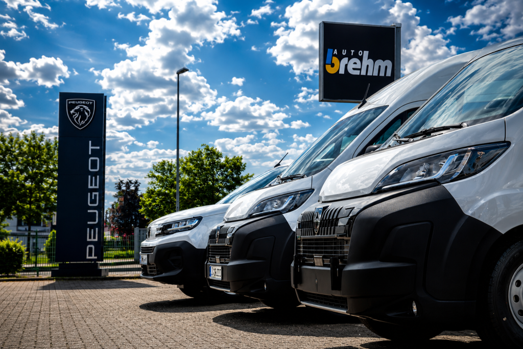 Mehrere Peugeot Professional Transporter stehen auf dem Hof von Auto Brehm mit Peugeot- und Auto-Brehm-Schildern im Hintergrund.